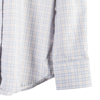 Close-up of a long-sleeve button-up shirt with a white base, light gray windowpane plaid, and thin orange grid lines, showing the fabric texture and cuff detail.
