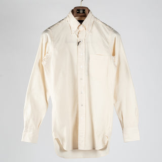 Drake's ecru pinpoint oxford button-down shirt shown front on, hanging on a wooden hanger against a pale grey backdrop.