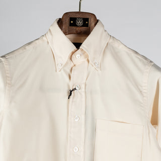 Drake's ecru pinpoint oxford button-down shirt in close up, with the collar points buttoned down over the placket.