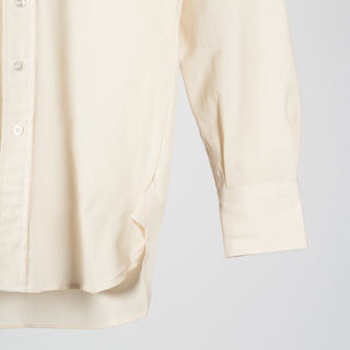 Drake's ecru pinpoint oxford button-down shirt from the side, showing the sleeve, single rounded cuff and curved hem.