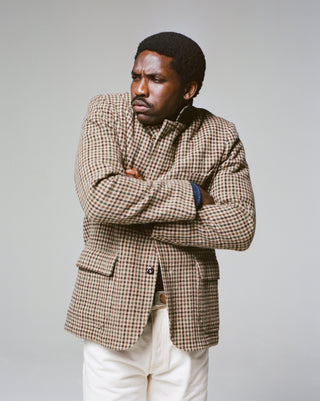 A model wears Drake's Brown and Green Houndstooth Tweed Games Blazer with arms crossed, paired with cream trousers.