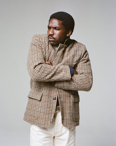 A model wears Drake's Brown and Green Houndstooth Tweed Games Blazer with arms crossed, paired with cream trousers.