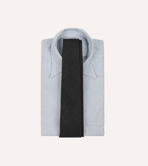 Drake's oxford weave wool tie laid over a folded blue striped oxford button-down shirt