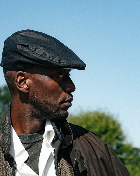 Barbour Black Cheviot Waxed Flat Cap worn in profile with a quilted gilet