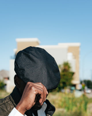 Barbour Black Cheviot Waxed Flat Cap, hand on the brim