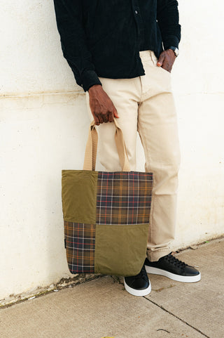 Barbour Dark Green Transport Patchwork Tote Bag carried with a black needlecord shirt and ecru jeans