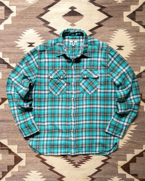 Wythe Thousand Lakes Plaid washed flannel pearlsnap shirt laid flat on a rug